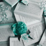 Open books laid one on top of another filling the scene. Flowers interspersed with the books.