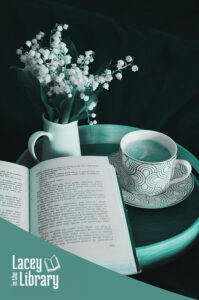 Open book rests against a round wooden tray holding a mug of coffee and a vase of tiny flowers. The image has a duotone treatment making the it appear in turquoise tones.