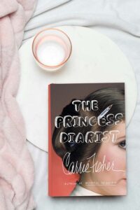 Flatlay of The Princess Diarist book and a cozy pink blanket and candle.