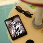 The long con book on kindle device in a beachy area