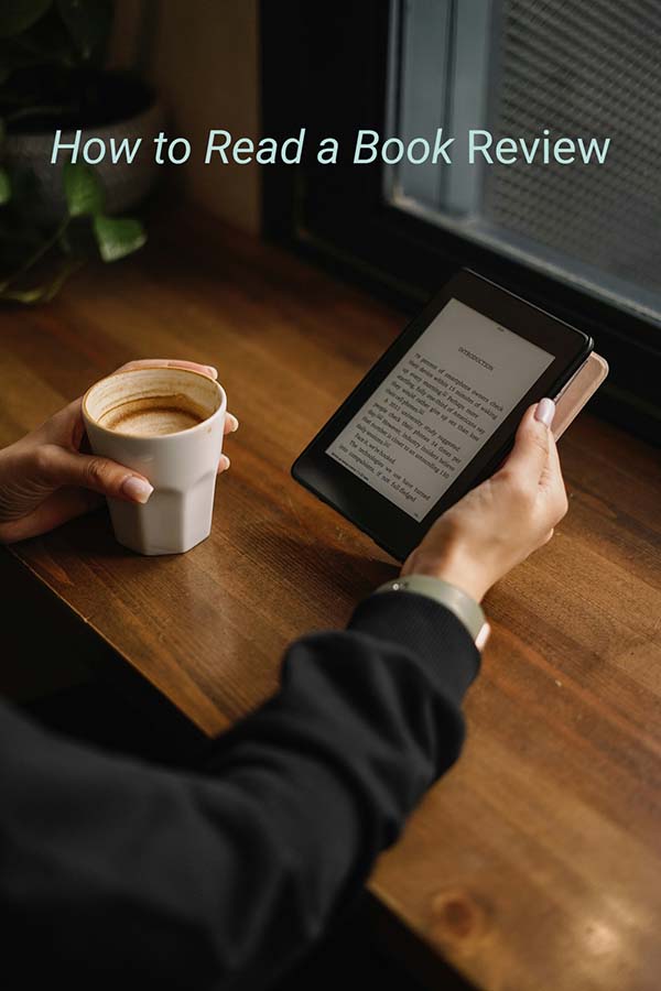 Hangs holding a coffee mug and an ereader at a table near a window