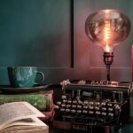 Typewriter, book, Edison bulb lamp and tea with both stacked and open books