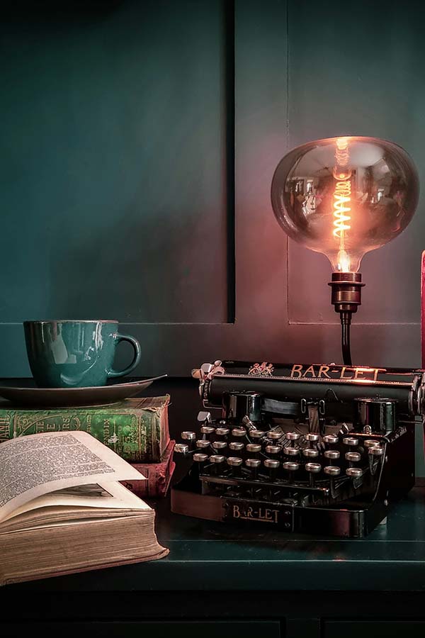 Typewriter, book, Edison bulb lamp and tea with both stacked and open books