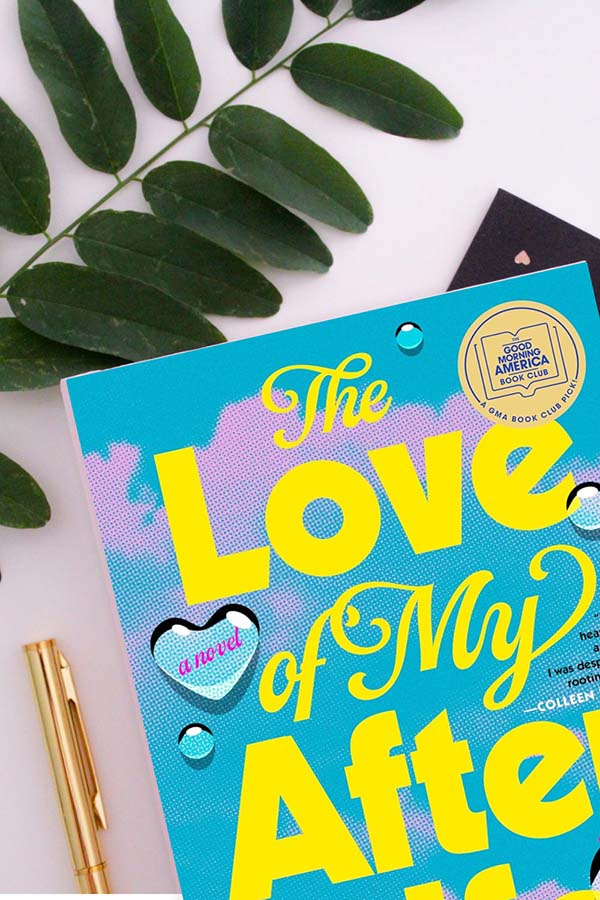 Flatlay of The Love of My Afterlife by Kirsty Greenwood with a plant, a notebook, and a pen
